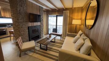 Una sala de estar moderna con chimenea de piedra, televisor de pantalla plana, sofá y comedor con cocina al fondo.