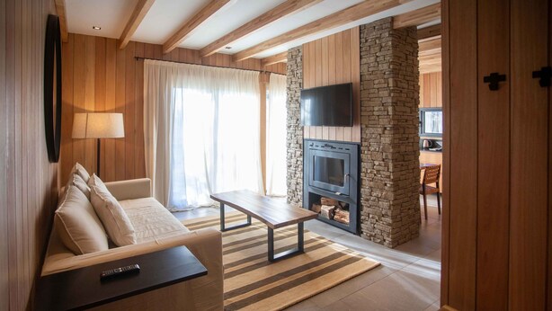 Un salon chaleureux avec une cheminée en pierre, un canapé, une table basse et un téléviseur fixé au mur.
