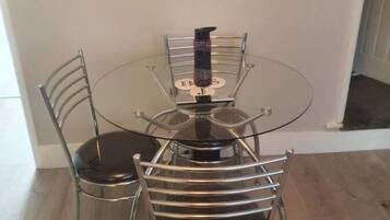 A round glass dining table with four metal chairs, a black bottle, and a small round table on the table.