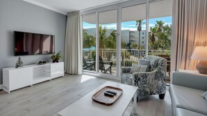 A modern living room with a flat-screen TV, a white console, a coffee table, and a patterned armchair. - Waterscape 3rd Flr  1 Bedroom with Courtyard views - on the beach - (Ft Walton Beach)
