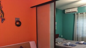 Een kamer met een bank, een kleine tafel, een bed met een grijze dekbedovertrek, en een airconditioning op de muur.