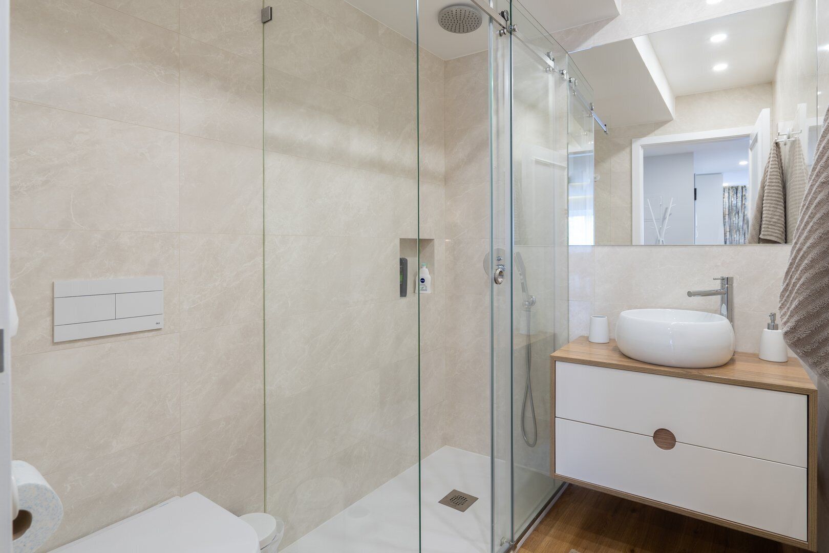 Une salle de bain moderne avec une douche à parois de verre, un lavabo blanc et un meuble-lavabo en bois.