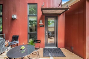 Un bâtiment rouge avec une porte noire, un petit jardin et une table avec des chaises à l’extérieur.