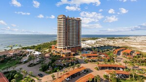 Un hotel de gran altura con vistas a la playa, que cuenta con un patio central con palmeras y zonas de estar al aire libre.