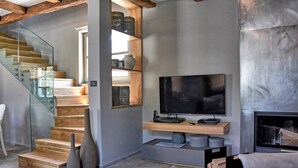 Un soggiorno moderno con una scala in vetro, una TV a schermo piatto montata su una mensola in legno e un camino.