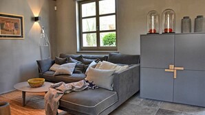 Un soggiorno moderno con un divano grigio, un tavolino rotondo, un mobile contenitore con motivo a croce e una finestra vista verde.