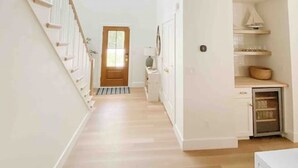 Un vestíbulo espacioso con una escalera de madera a la izquierda, una puerta al final y un armario empotrado con estantes a la derecha.