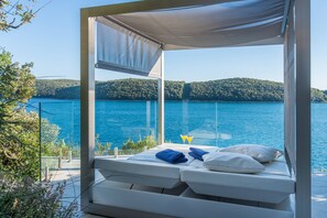 A bed with a canopy overlooking a lake with hills in the background.