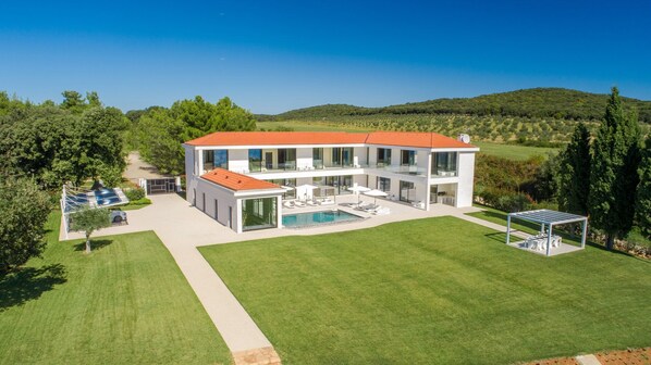 A modern two-story house with a swimming pool, a covered outdoor seating area, and a well-maintained lawn.