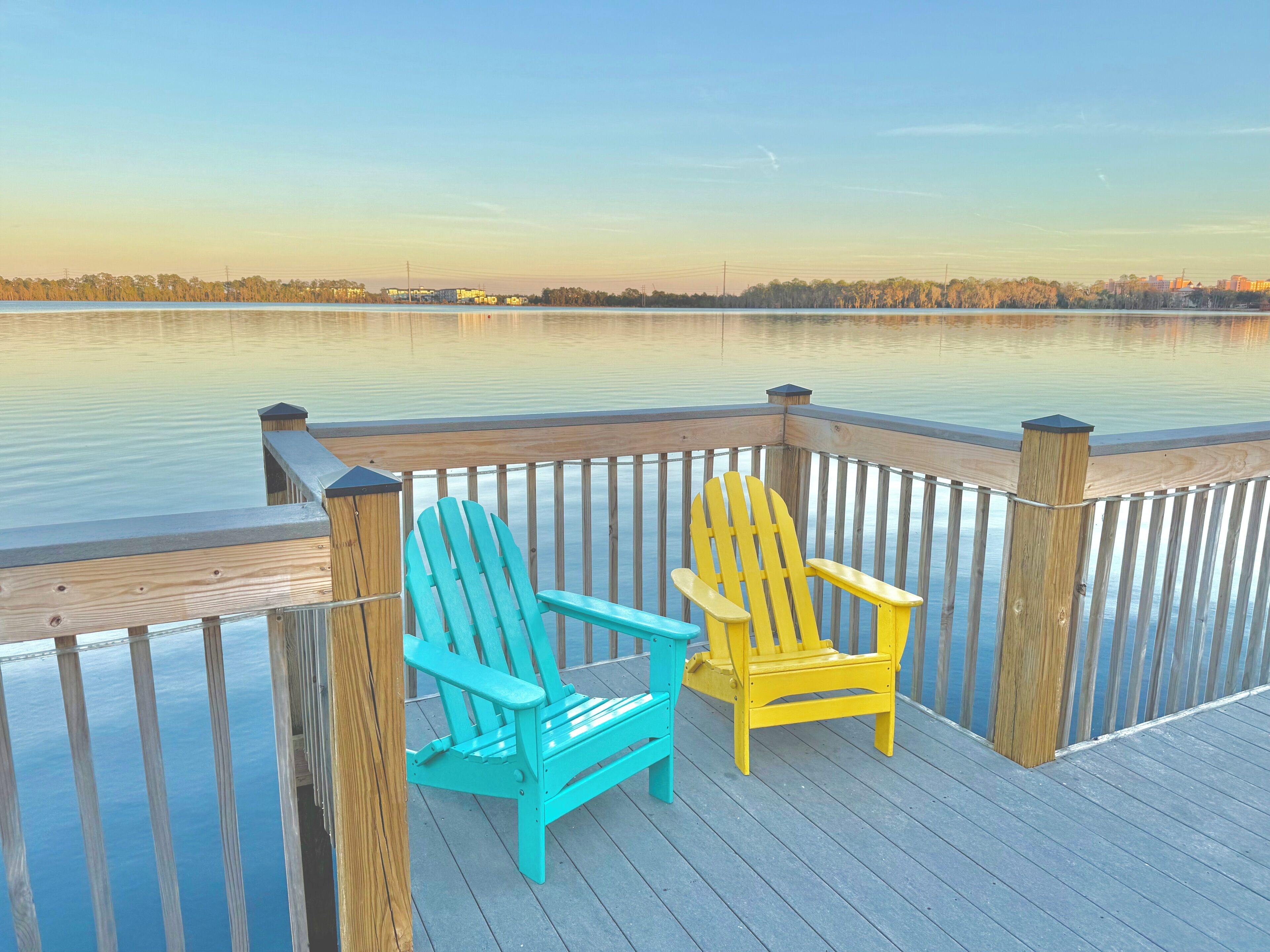Een houten terras met twee Adirondack-stoelen uitkijkend op een rustig meer.