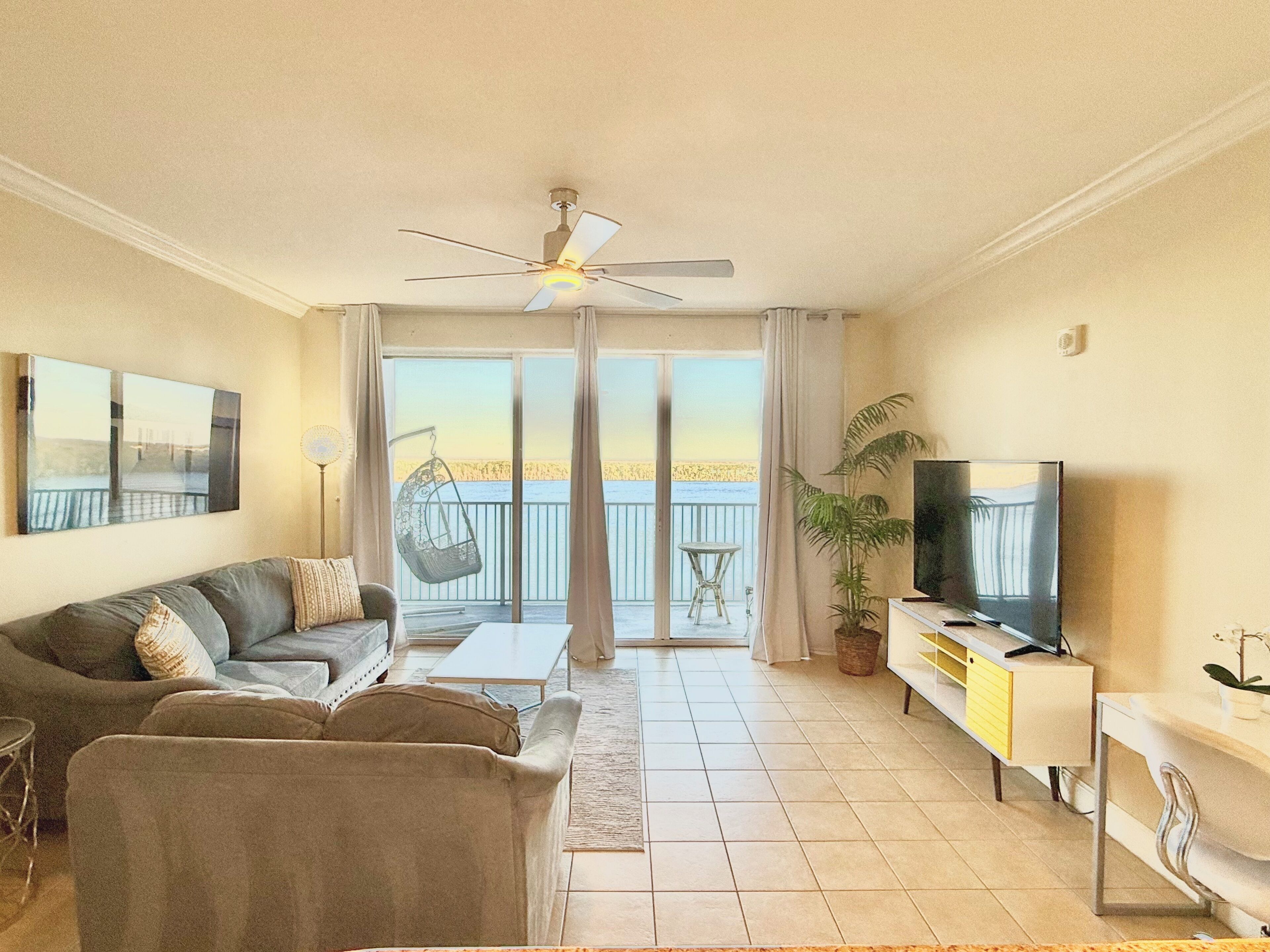 Ein Wohnzimmer mit einer Couch, einem Fernseher, einem Deckenventilator, einem Balkon mit Blick und einem Essbereich.