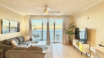 Ein Wohnzimmer mit einer Couch, einem Fernseher, einem Deckenventilator, einem Balkon mit Blick und einem Essbereich.