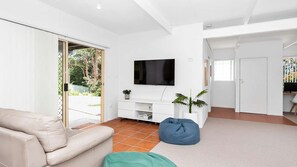 A modern living room with a sofa, a blue bean bag, a TV, and a sliding glass door leading to a balcony.