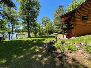 A log cabin with a deck, a pond, and a grassy area with trees.