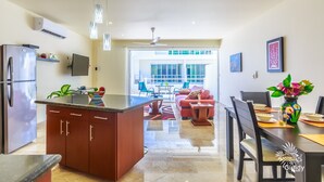 Een moderne keuken met een centraal eiland, een eethoek met een tafel en stoelen, en een woonkamer met een bank en een televisie.