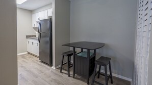 Una cocina compacta con un refrigerador empotrado, una mesa de madera oscura con dos taburetes y un ventilador de techo.