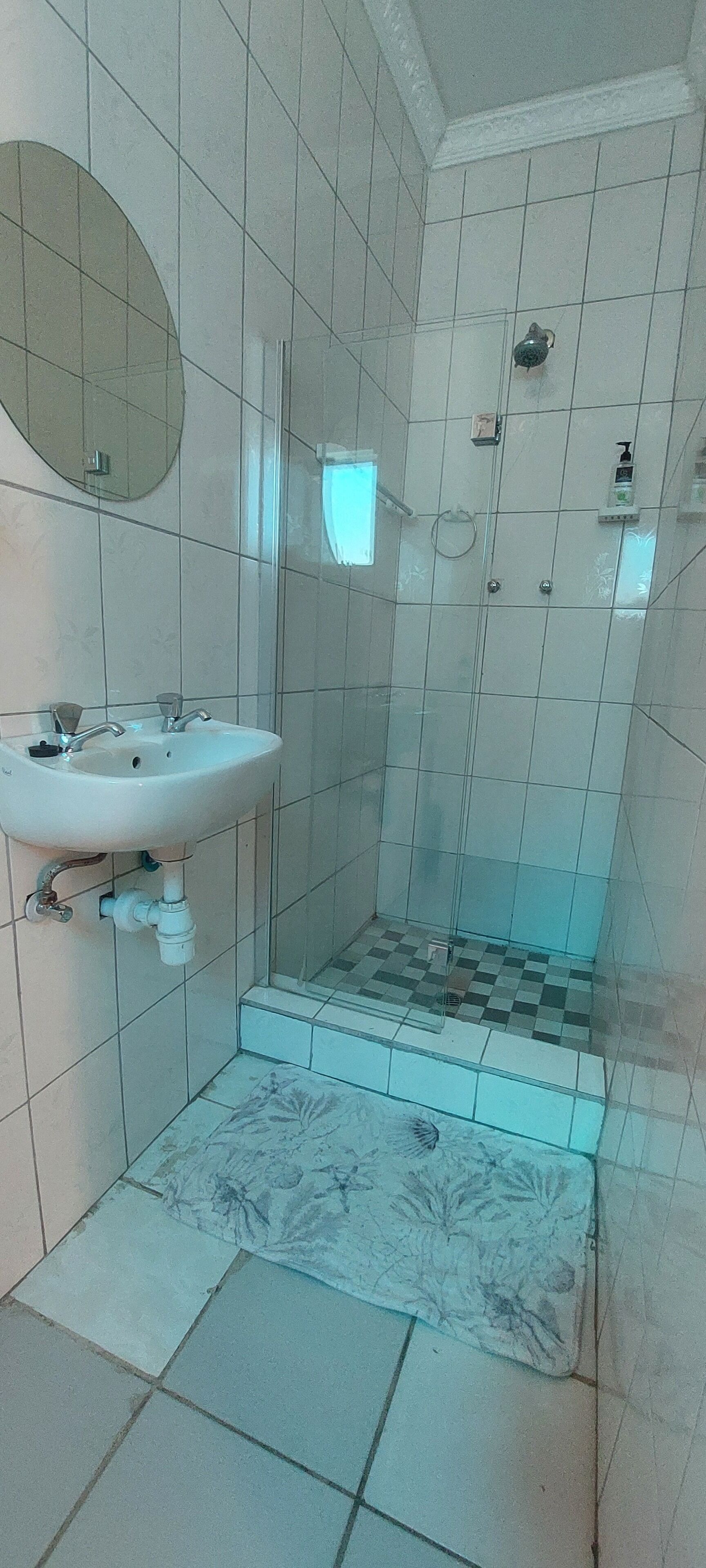 Ein Badezimmer mit Waschbecken, Spiegel, Dusche und Fliesenboden.