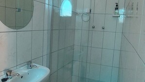 A bathroom with a sink, mirror, shower, and tiled floor. - Family room (Khomasdal)