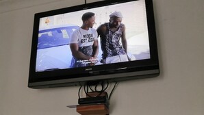 A television mounted on a wall displaying two people. - Family room (Khomasdal)
