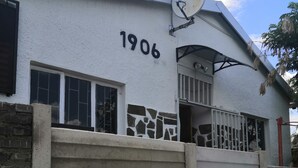A white building with the number 1906, a satellite dish, and a gated entrance. - Family room (Khomasdal)