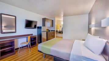 A hotel room with a bed, a desk, a chair, a television, and a kitchenette.