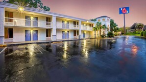 Et motel med flere værelser, en parkeringsplads og en bygning med et '6'-tal i baggrunden.