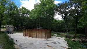 Un patio de piedra con un jacuzzi de madera rodeado de árboles.