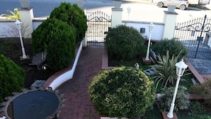Een verharde tuin met een decoratieve fontein, diverse struiken en een metalen poort.