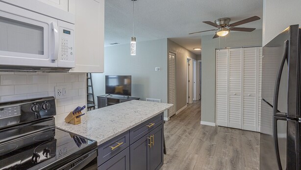 A modern kitchen with white cabinets, a black stove, a microwave, and a refrigerator. There is a wooden countertop and a ceiling fan.