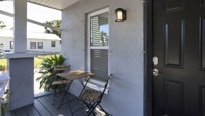 A porch with a wooden table and chairs, a door, and a window with shutters.