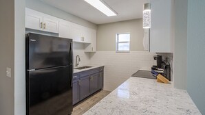 A modern kitchen with white cabinets, a black refrigerator, a marble countertop, and a window providing natural light.