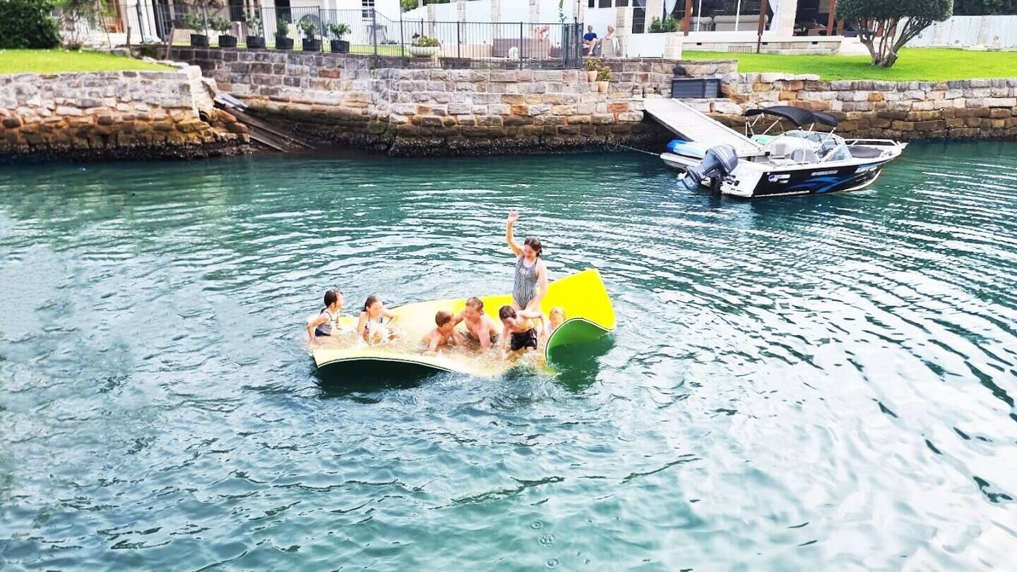 Un grupo de personas en un bote inflable amarillo en el agua, con un muelle y una embarcación al fondo.