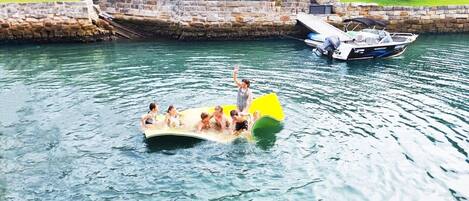 Un grupo de personas en un bote inflable amarillo en el agua, con un muelle y una embarcación al fondo.