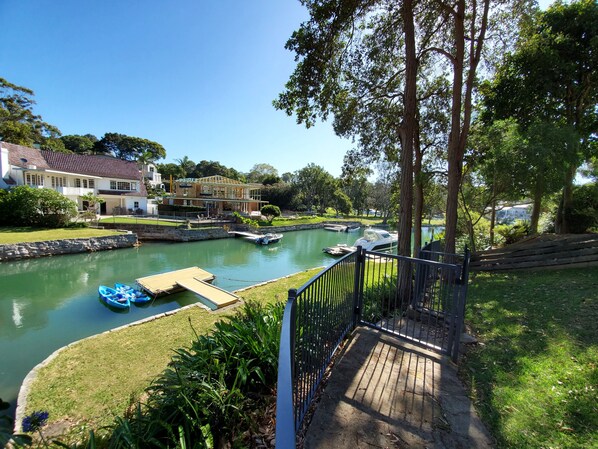A riverside property with a dock, boats, and a house with a garden.