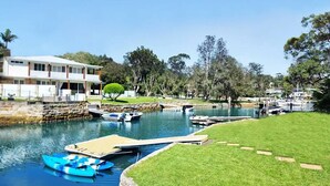 A waterfront property with a house, a dock, and a small boat. - Holiday on the Waterfront in Pittwater -Beach, Swim, Kayak, Boat, Fish and More! (Newport)
