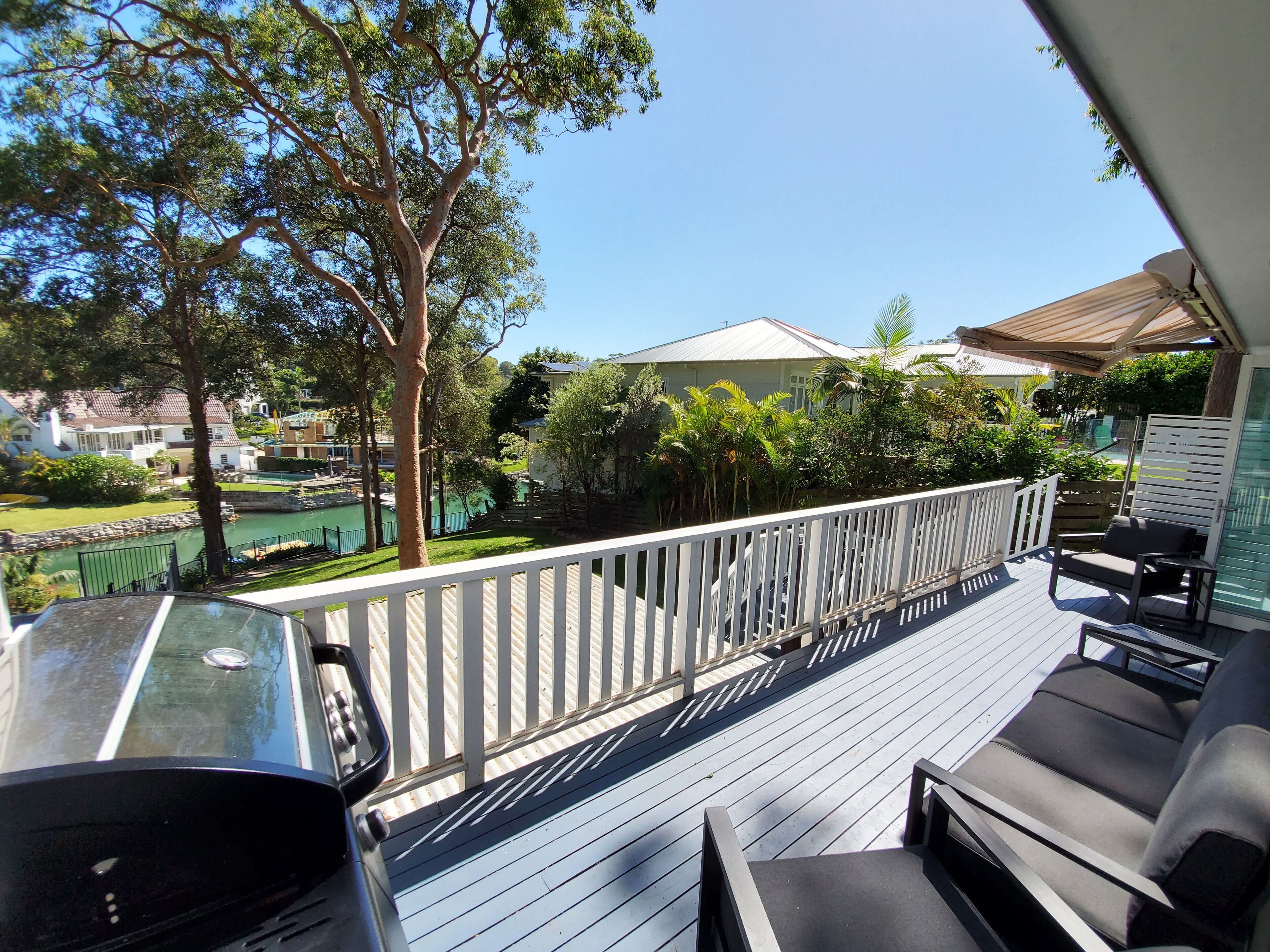 A deck with outdoor furniture, a white railing, and a view of a residential area with houses and greenery.