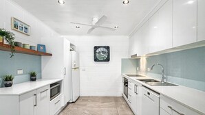 Une cuisine moderne avec des meubles blancs, un four encastré, un four à micro-ondes, un lave-vaisselle et un ventilateur de plafond.