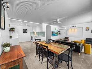 A modern kitchen with white cabinets, a dining area with a wooden table and chairs, and a living area with a sofa and a TV.