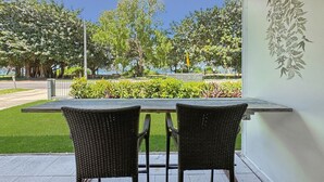 Une terrasse couverte, agrémentée de deux fauteuils en osier et d’une table, qui offre une vue sur un jardin bien entretenu et une route.