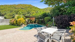 Un jardin avec une piscine, du mobilier de jardin et une vue sur une colline boisée.