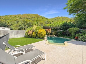 A backyard with a swimming pool, a grassy lawn, and a wooden fence.