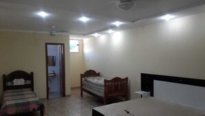 Une chambre avec deux lits, un ventilateur de plafond, des spots encastrés et une porte donnant sur une salle de bain.