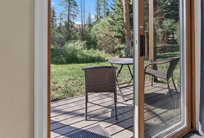Una terraza con mesa y sillas, con vista a una zona verde con árboles.