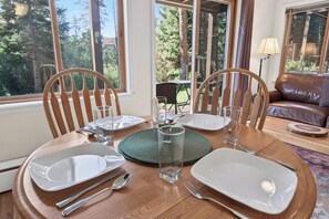 Mesa de comedor dispuesta para cuatro personas, con sillas, vaso, platos, cubiertos y posavasos.