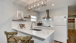 Une cuisine moderne avec un îlot central blanc, des appareils en acier inoxydable et des chaises en bois.