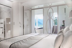 A modern hotel room with a bed, a bathroom with a glass shower enclosure, and a balcony with a view of the mountains. - Impérial Palace (Annecy)