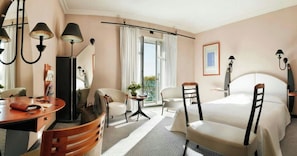 A hotel room with a bed, a desk, a chair, a small table, and a balcony with a view. - Impérial Palace (Annecy)