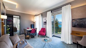 A hotel room with a dining area, a red armchair, a sofa, a TV, and a balcony with a view. - Impérial Palace (Annecy)