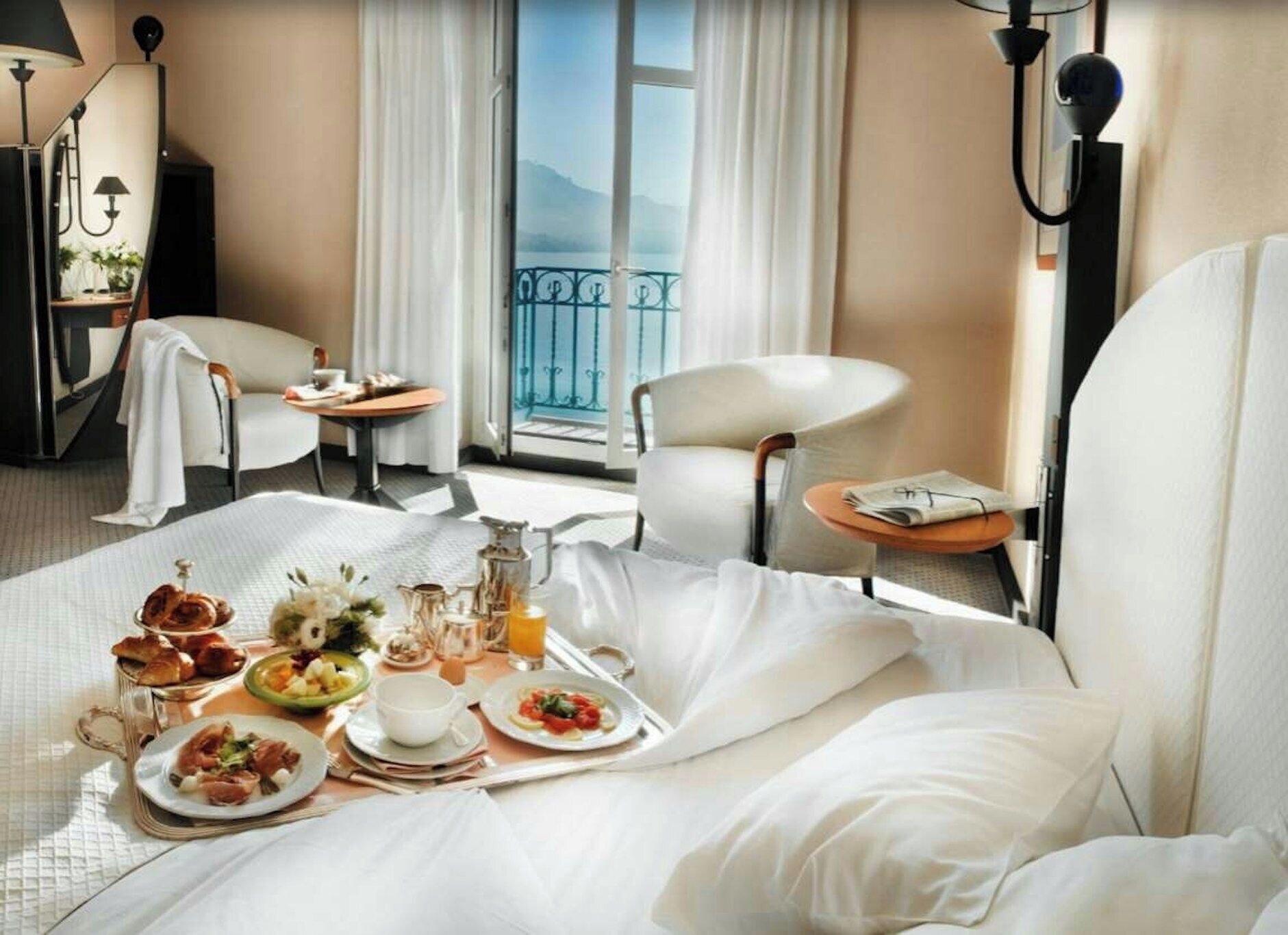 A hotel room with a bed, breakfast tray, two chairs, a table, and a view of the outdoors.