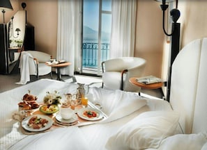 A hotel room with a bed, breakfast tray, two chairs, a table, and a view of the outdoors. - Impérial Palace (Annecy)